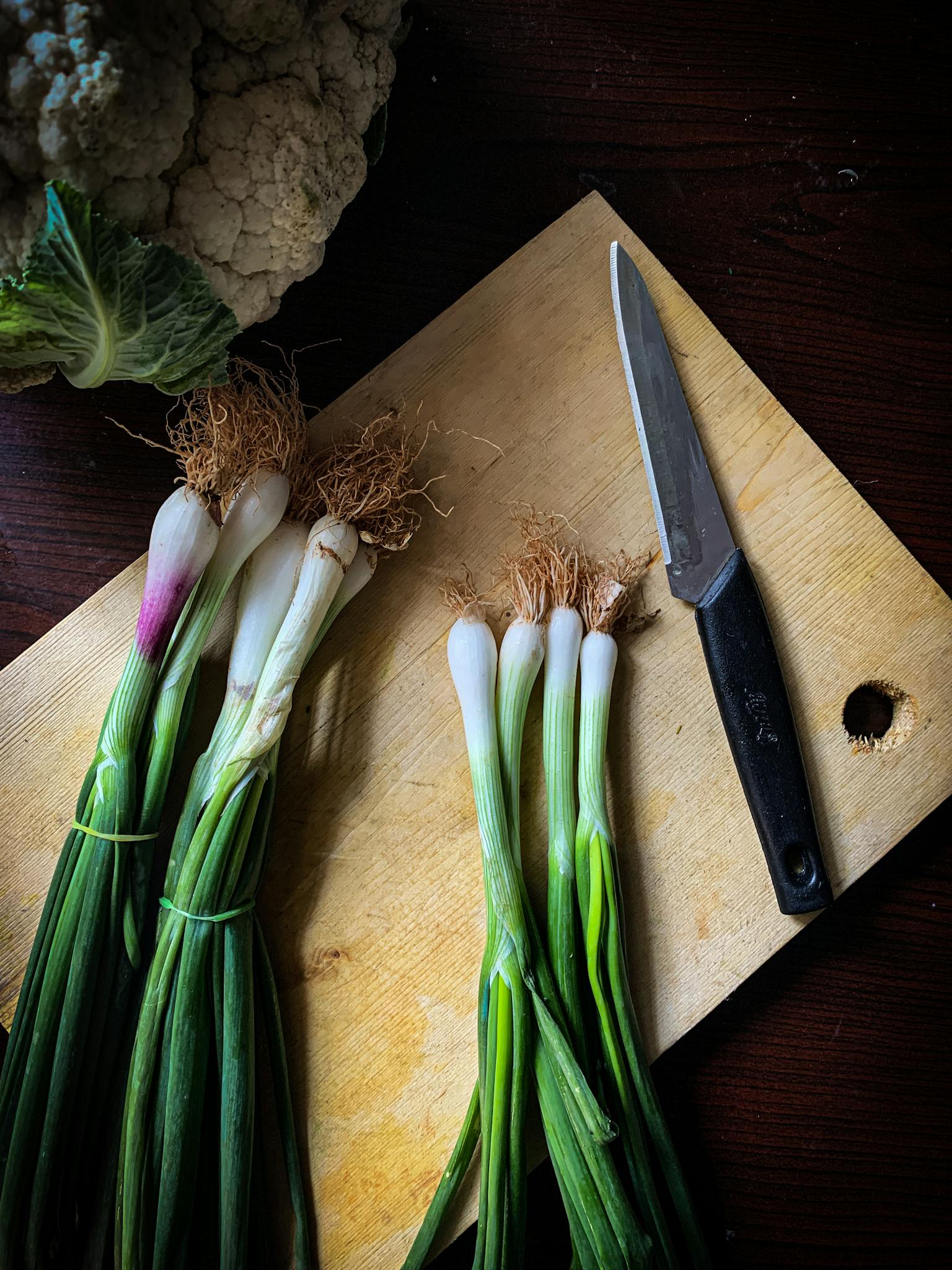 Close-up of fresh onions, cauliflower, and a knife on a rustic wooden board. Perfect for healthy lifestyle themes.